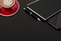 Selected focus black spiral notebook black pen ,smartphone and red cup of coffee on black desk Royalty Free Stock Photo