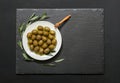 Selected olives in a white plate decorated with natural olive tree branches on a dark background.