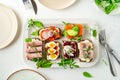 Selection of Danish smorrebrod open sandwiches on a platter, salad leaves, plates, cutlery on white background Royalty Free Stock Photo