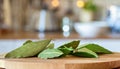 A selection of fresh herbs: bay leaves, sitting on a chopping board against blurred kitchen background copy space