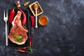 Raw steaks and frying pans with seasoning, garnishes and ingredients on a dark rustic background with copy space. Royalty Free Stock Photo