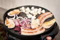 Selection of meat grilling on a electric portable barbecue with sausages, champignons and onion. BBQ season. Royalty Free Stock Photo