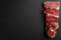 Selection of raw beef meat food steaks against black stone background.