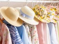 A selection of stylish summer hats paired with floral and pastel dresses hanging on a white rack.