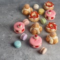Selection of various pieces of cake - Choux pastries, macarons, chocolate velvet cake on a gray stone background.