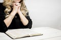 Selective closeup shot of a female praying with tightly linked fingers near an open book on a table Royalty Free Stock Photo