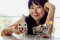 Selective focus of asian woman`s hand holding a wooden house model with full of coins in shopping cart Royalty Free Stock Photo