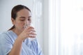 Selective focus on Asian young patient woman`s hand holding a glass of water. She is drinking pure water at hospital bed Royalty Free Stock Photo