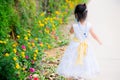 Selective focus. Back view of girl in a beautiful dress is walking on the street. Along the street road planted colorful flowers.