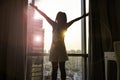 Back view young woman which she is looking at dawn city scenery and stretch the muscles at window. Health