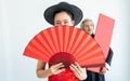 Selective focus beautiful happy Asian rich woman wearing red qipao or dress, smiling, holding folding fan with blur male bodyguard