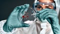 Selective focus of biochemist in hazmat suit holding petri dish with biomaterial