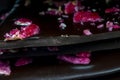 Selective focus. Black chocolate tile with red dried and fresh berries and candied flower leaves. Black background, close up Royalty Free Stock Photo