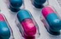 Selective focus of blue, pink capsule with granule in side pills. Pills in blister pack on white background. Pharmaceutical dosage