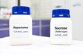 Selective focus of a bottle of pure aspartame artificial sweetener and sucrose or table sugar chemical compound comparison.