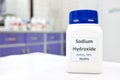 Selective focus of a bottle of pure sodium hydroxide or NaOH chemical compound beside a petri dish with white solid pellets. Royalty Free Stock Photo