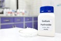 Selective focus of a bottle of pure sodium hydroxide or NaOH chemical compound beside a petri dish with white solid pellets. Royalty Free Stock Photo