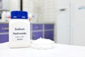 Selective focus of a bottle of pure sodium hydroxide or NaOH chemical compound beside a petri dish with white solid pellets. Royalty Free Stock Photo