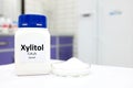 Selective focus of a bottle of pure xylitol sugar substitute with powder in petri dish. White laboratory background