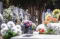 selective focus of a bouquet of plastic flowers on a cemetery grave, out of focus around colorful bouquets of natural flowers, all