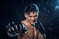 Selective focus on boxer in leather gloves standing under water drops on black.