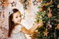 Selective focus. A brunette girl in a silver dress decorates a Christmas tree with a ball on the background of lights of garlands Royalty Free Stock Photo