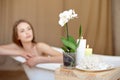 Selective focus of candles and flowers on the wooden table in spa salon with blurred woman on background. Royalty Free Stock Photo