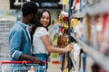Focus of cheerful african american man standing with cheerful asian girl smiling near groceries in supermarket Royalty Free Stock Photo