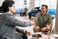 Selective focus of cheerful customer male purchasing automobile in dealership signing paper shaking hands with dealer