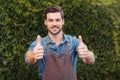 Cheerful gardener in apron showing thumbs up and looking at camera