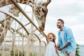 selective focus of cheerful man and kid with closed eyes feeding giraffe in zoo.