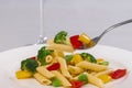 Close up of a fork holding pasta and vegetables over an out of focus pasta salad plate Royalty Free Stock Photo