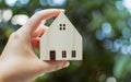 Selective focus and close up on hand holding mini model figure of house or home with blur background of tree. Presenting about Royalty Free Stock Photo