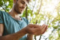 Selective focus. Close up portrait of young dark-skinned male with beard in blue shirt holding little plant in hands Royalty Free Stock Photo