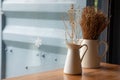 Selective focus and close up shot of cafe decorating with dried flowers in white ceramic jar on the wooden table near the glass