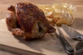 Select focus of a spit-roasted chicken on a wooden board with an out of focus bag of potato chips Royalty Free Stock Photo