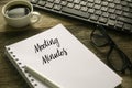 Selective focus of coffee,computer keyboard,glasses,pen and notebook written with Meeting Minutes on wooden background