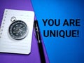 Selective focus.Compass on a notebook with pen and word YOU ARE UNIQUE on a colorful background.