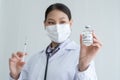 Selective focus on Covid-19 vaccines vial bottle in hand of Asian young doctor woman with face mask, stethoscope holding syringe Royalty Free Stock Photo