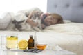 Cup of tea, lemon and medicines for colds or allergies on foreground, a girl in a sweater laying on a bed Royalty Free Stock Photo