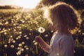 Selective focus cute blonde curly hair girl blowing blossomed dandelion flower head  seedlings fly away. Royalty Free Stock Photo