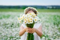 Selective focus. Cute girl with a bouquet of chamomile flowers and a wreath of daisies on her head in a field, holding a bouquet