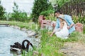 selective focus of cute kid in dress and straw hat sitting near happy father and lake with black swans. Royalty Free Stock Photo