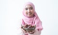 Selective focus on dry dates fruit in bowl. Asian 30s Muslim woman wearing traditional clothes with hijab, smiling holding energy Royalty Free Stock Photo