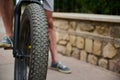 Shallow tread of a bicycle tubeless tire. Selective focus on e-bike wheel and feet on pedals of a male cyclist in denim
