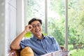 Selective focus at face. Senior Asian man reading newspaper mock up at the sofa couch while drinking coffee in the morning. Happy Royalty Free Stock Photo