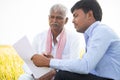 Selective focus on farmer, Bank officer explaning about farm loan paper documents to Indian farmer near agriculture field -