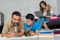 selective focus of father and son doing homework together while mother and daughter using laptop on sofa Royalty Free Stock Photo