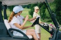 selective focus of female golfers in caps in golf cart greeting friend with golf gear