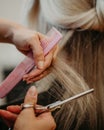 Selective focus of a female hairdresser with scissors and comb cutting blonde hair in a salon Royalty Free Stock Photo